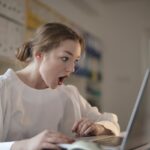 Surprised woman sitting at desk with laptop indoors, expressing amazement.